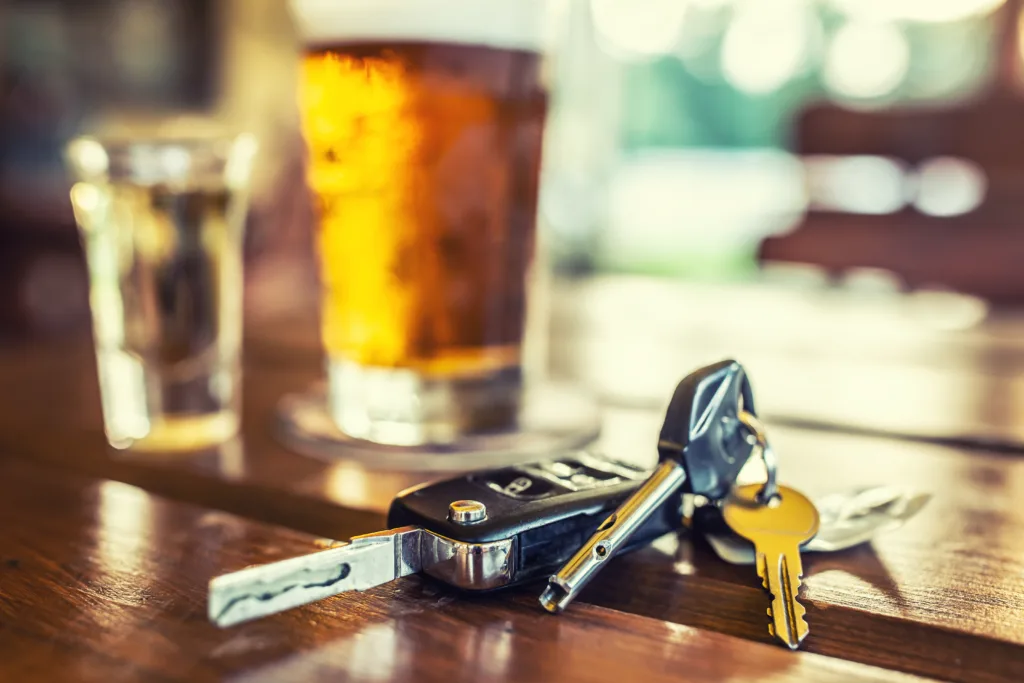 Car keys and glass of beer or distillate alcohol on table in pub or restaurant.