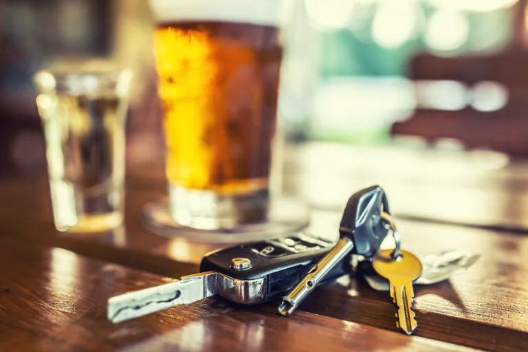Car keys and glass of beer or distillate alcohol on table in pub or restaurant.